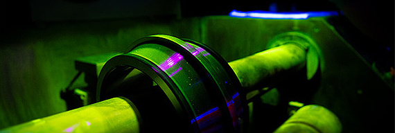 Magnetpulverprüfung von einem Innenring Hintergrund in schwarz; neonleuchtendes Violett, Grün und Blau: Der Innenring eines Pendelrollenlagers wird einer Magnetpulverprüfung unterzogen.